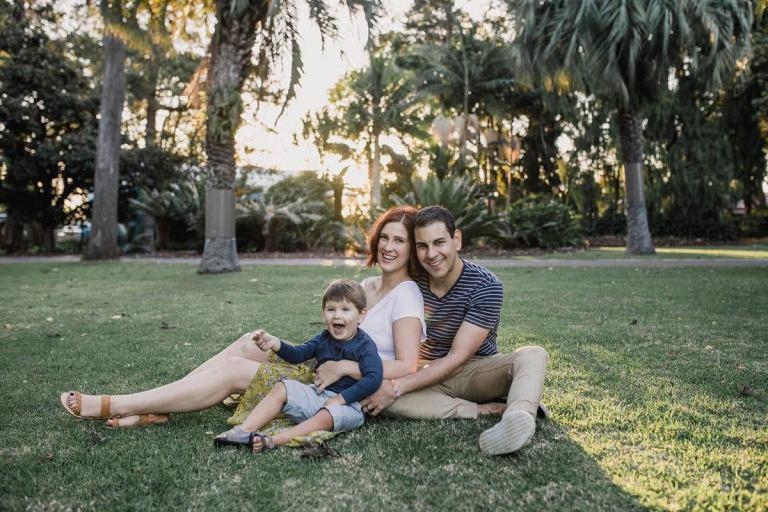 A family enjoying a sunny day, sitting together on the grass in a park, surrounded by trees and nature.