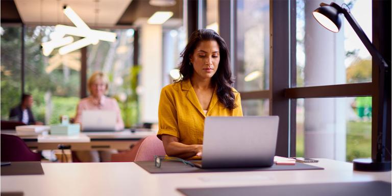 A woman focused on her laptop, diligently working in a modern office environment.
