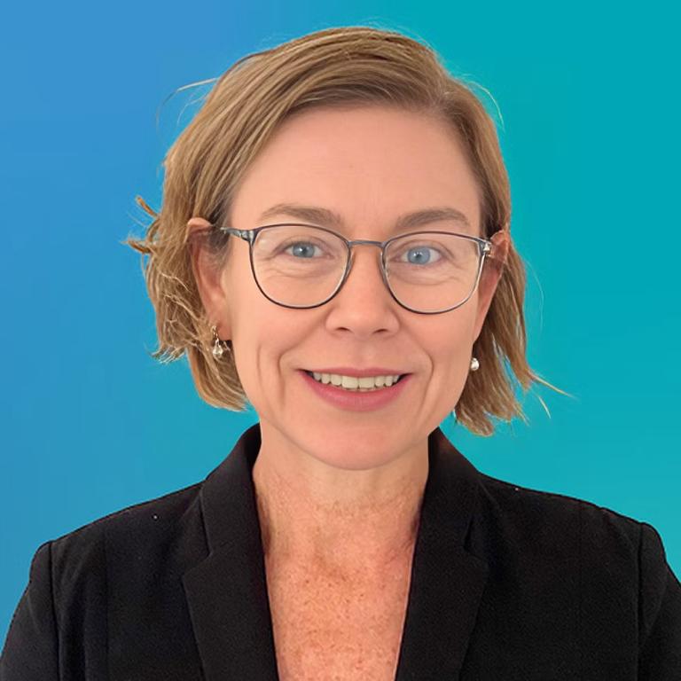 A woman wearing glasses and a black blazer smiles warmly, exuding confidence and professionalism.