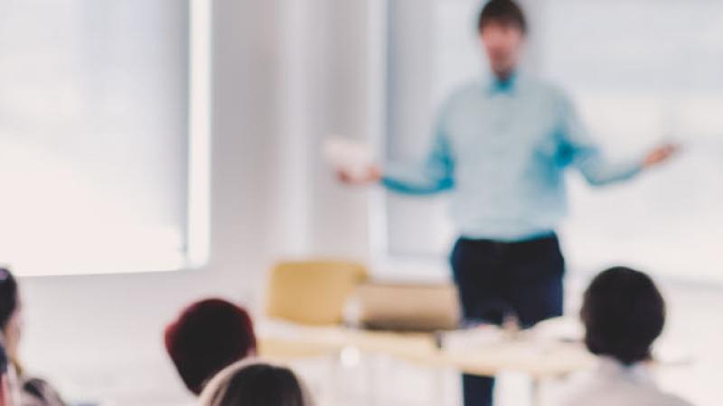 A man stands at the front, presenting to an engaged audience of diverse individuals seated in a conference room.