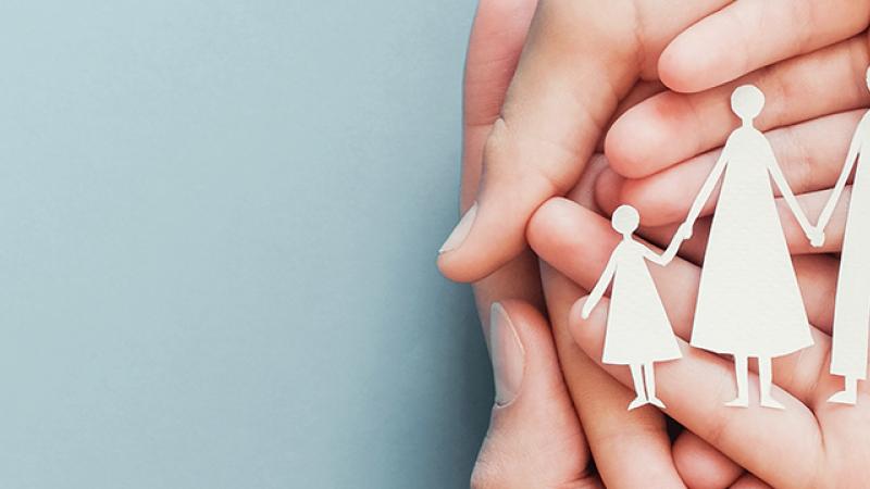 A person's hands hold a paper cutout of a family, symbolizing unity and togetherness in a heartfelt display.