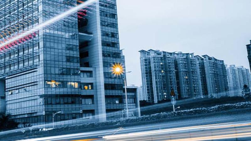 A bustling city street lined with tall buildings and parked cars, showcasing urban life and architecture.