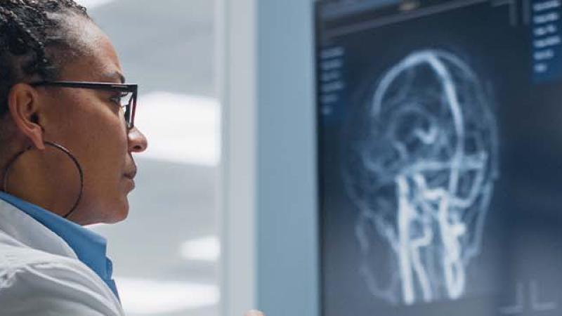 A woman in a lab coat examines data displayed on a computer screen in a laboratory setting.