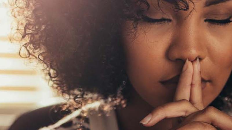 A woman with her hand on her mouth and a finger to her lips, signalling for silence or contemplation.