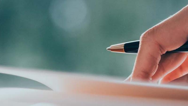 A person writing on paper with a pen, focused on their task, showcasing the act of note-taking or drafting.