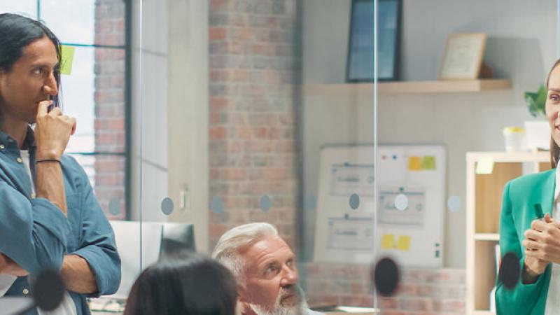 A diverse group of professionals collaborates in an office, surrounded by colorful sticky notes on the wall.