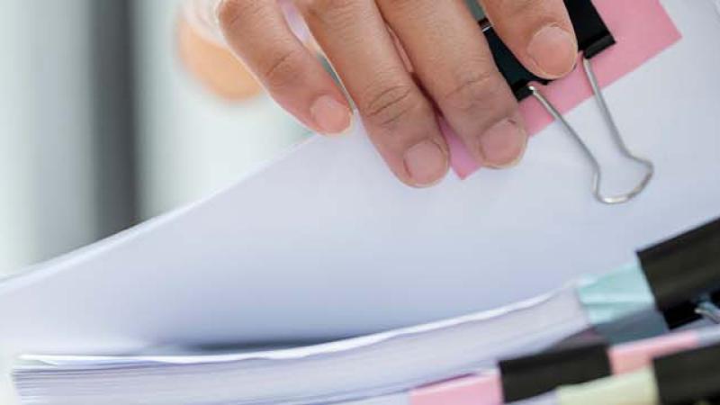 A person holds a neatly organized stack of papers secured with a clip, showcasing a professional and tidy appearance.