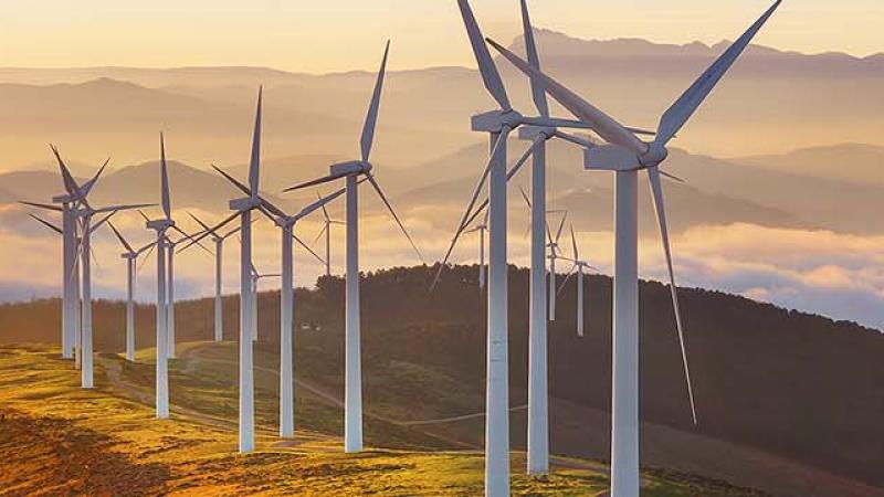 Wind turbines atop a mountain, surrounded by clouds, showcasing renewable energy in a scenic landscape.