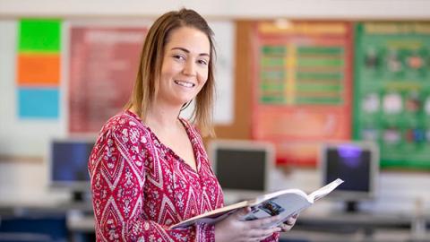 A woman smiles brightly while holding a book, radiating joy and enthusiasm for reading.