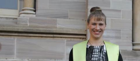 A woman in a graduation gown beams at the camera, celebrating her academic achievement with a joyful smile.
