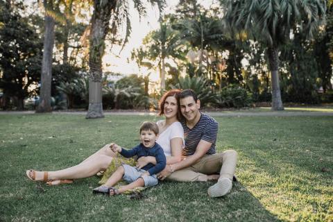 A family enjoying a sunny day, sitting together on the grass in a park, surrounded by trees and nature.
