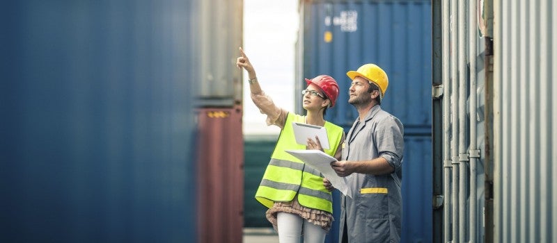 A male and female engineer wearing hard hats and pointing at a building.