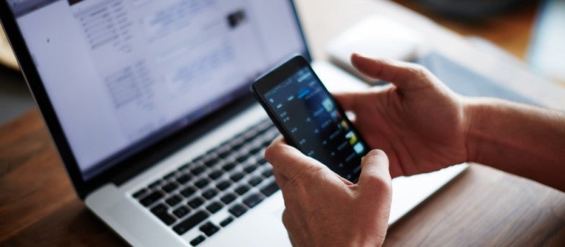 An accountant holding a smartphone next to laptop. 