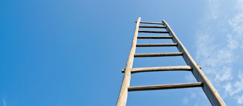 A empty wooden ladder pointing up to a clear blue sky.