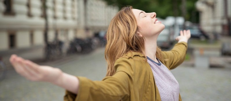 A woman smiling with open arms, looking up to the sky. 