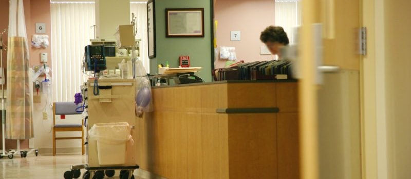 A hospital ward with a nurse standing behind a desk.