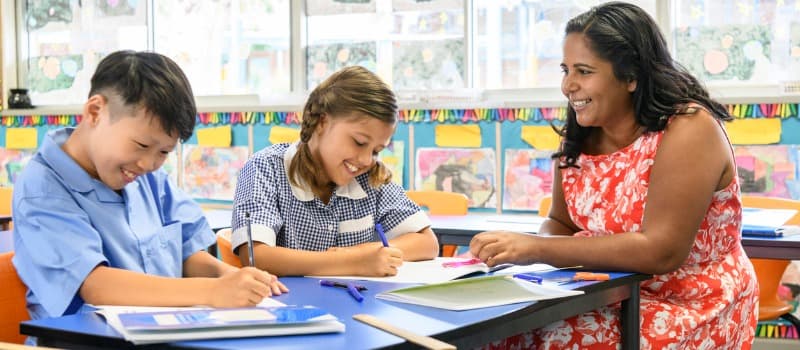 A teacher sitting in a classroom with two of her students.